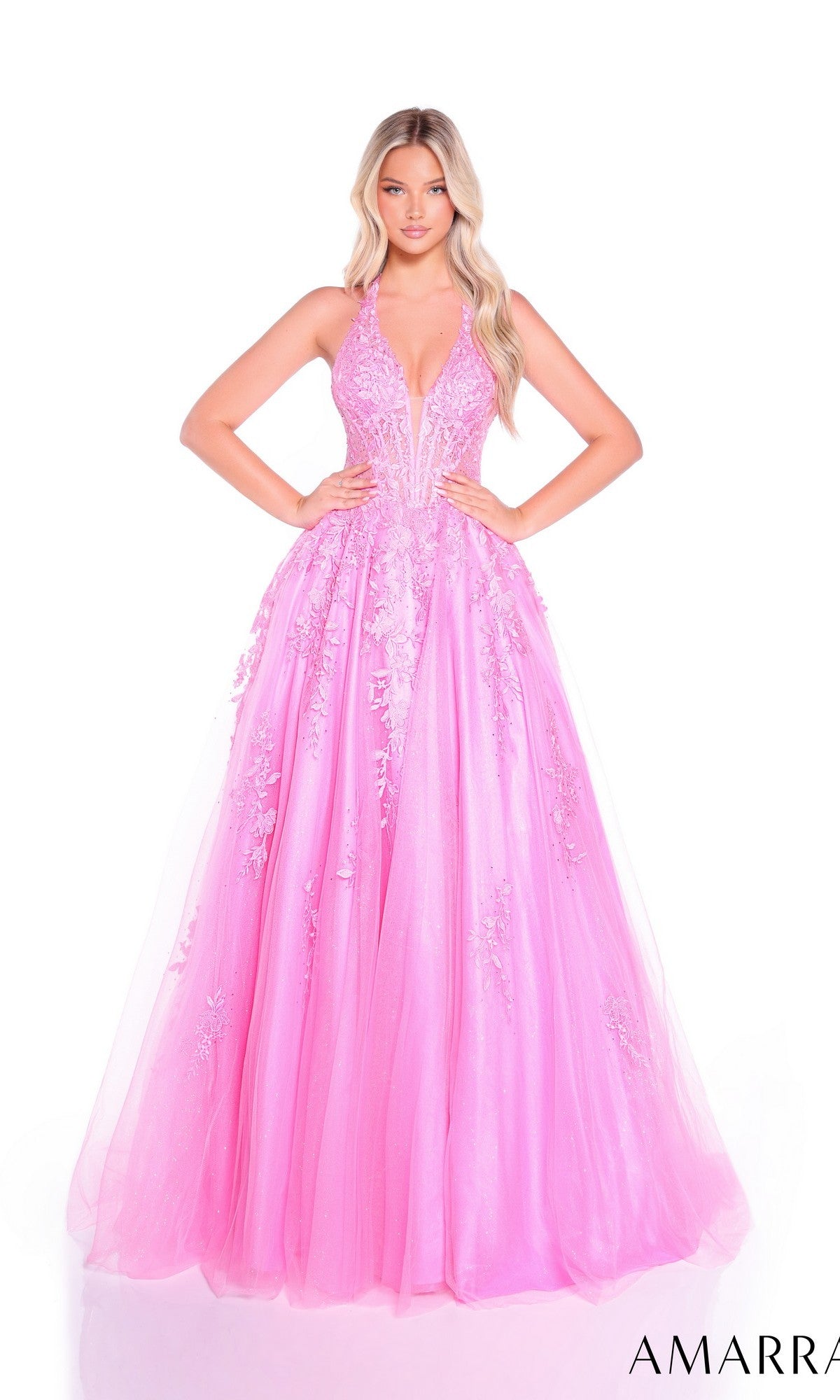 A woman stands with her hands on her hips against a white background, wearing the Amarra 89317 long prom dress—a bright pink, floor-length gown with a lace-embroidered bodice and floral embellishments.